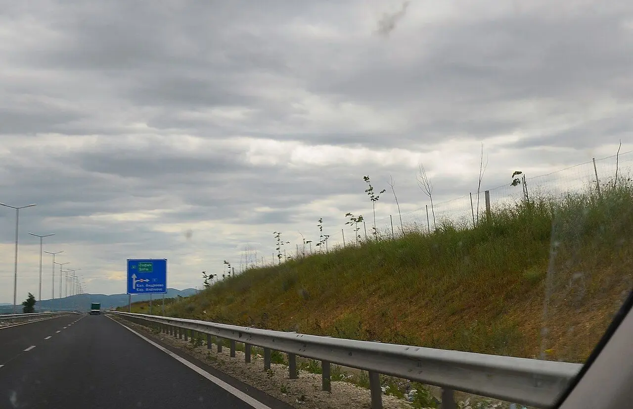 Maritsa motorway under cloud, with a blue direction sign and lighting columns.
