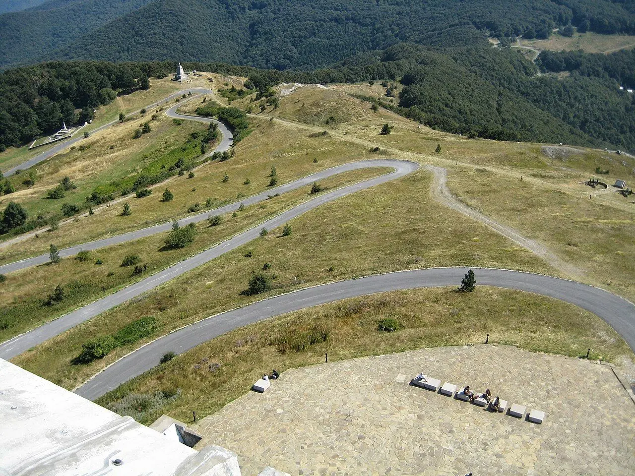 Switchbacks on the road to Shipka Pass, bare grass and forested slopes.