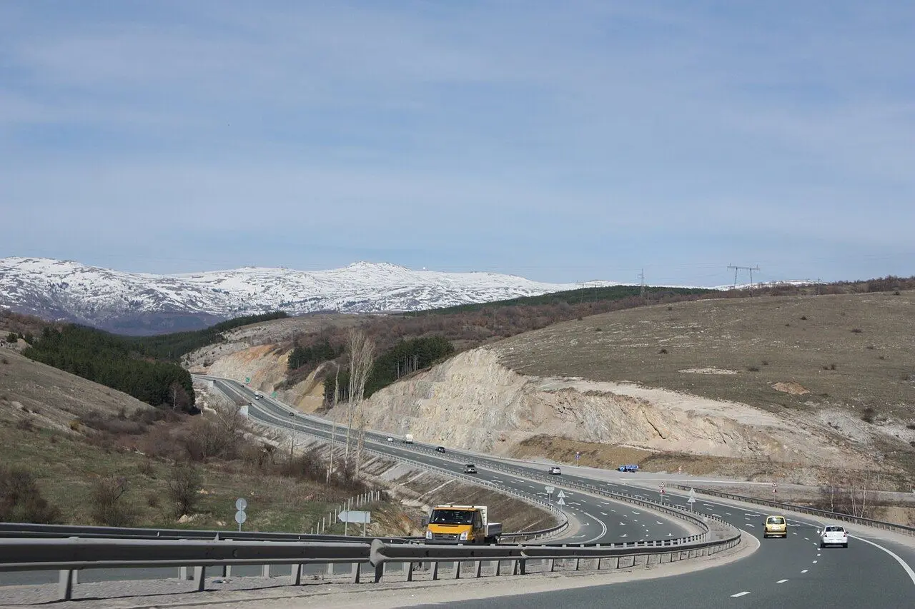Struma motorway curving through hills north of Sofia, with snow on the ridge beyond.